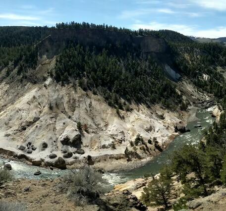 Panorama of a river in a canyon flowing around a barren hillside with some gas vents