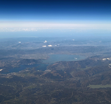 A photo taken from an airplane of a large, elongated lake surrounded by long mountain ridges and vineyards
