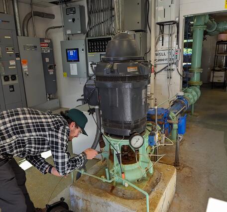 Man bent over lowering a measuring tape into an access pipe in a groundwater pump