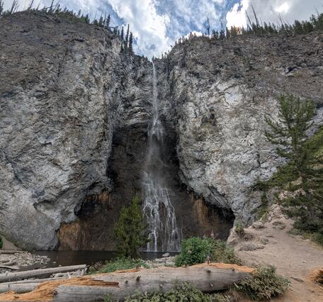 Ribbon-like waterfall on a gray cliff with a few trees and a splash pool in the foreground