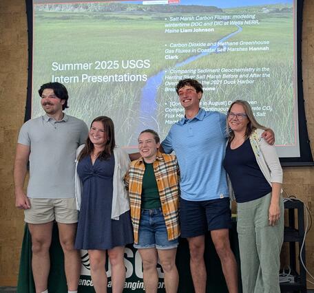 four people posing for photo together in front of PowerPoint presentation