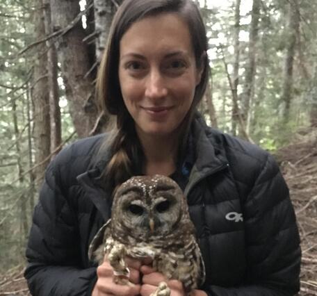 dark haired woman smiling in the forest gently holding an owl