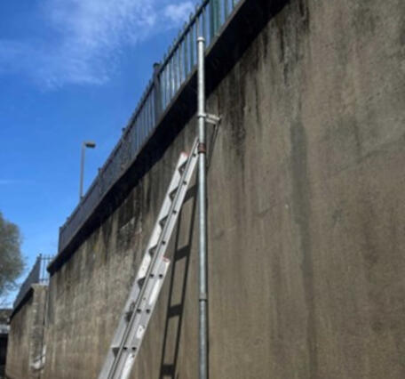 Steel pipe which monitors water level attached to the side of a bridge with a ladder next to it