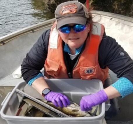 woman in sunglasses and hat and life jacket on boat holding a fish