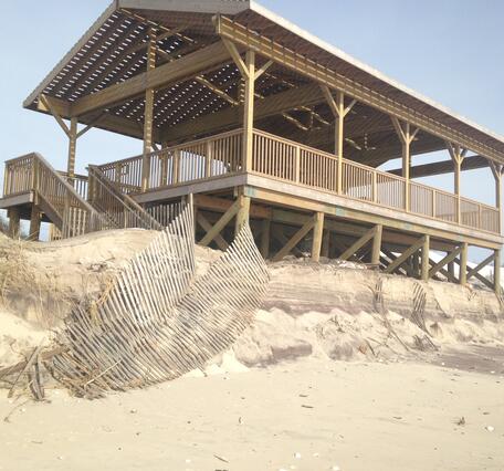 A pavilion on a beach at the edge of an eroded dune is partially covered by sand after a winter storm