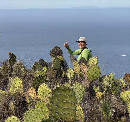 Biologist Sarah Birchard stands near prickly pear cacti and gives a thumbs up at Pyramid Point, San Clemente Island