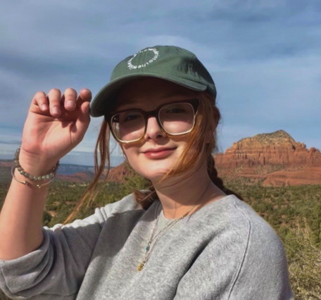 Person wearing glasses and green hat with dryland mountains and valleys
