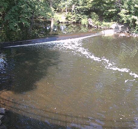 Looking upstream as water flows over teh small weir toward the viewer