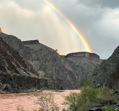 A rainbow in a stormy sky arches over Grand Canyon and the Colorado River