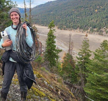 woman carrying rope and box with mountains in background