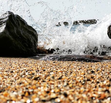 A wave crashes between two rocks on a sandy beach.