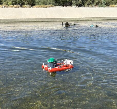 Bright red remote controlled ADCP boat floats in a canal at the Las Vegas Wasteway monitoring site.