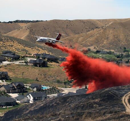 White airplane drops red fire retardant over the hills near a neighborhood