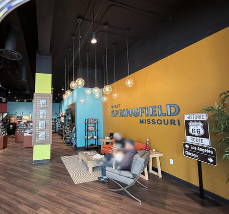 Wide view inside the visitor center, showing seating, merchandise displays, and a wall reading “Visit Springfield Missouri.” 
