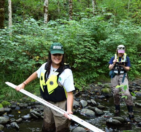 Scientists hold survey equipment in forested stream
