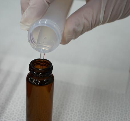 Close up view of gloved hand pouring water sample from plastic tube to glass bottle