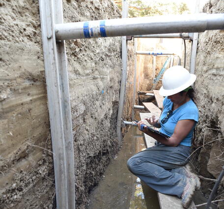 USGS scientist taking notes while seated on scaffolding inside a deep paleoseismic trench cut into the San Andreas fault.