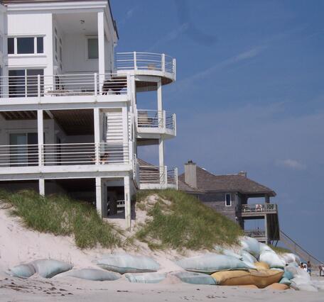 Sandbags partially shore up a badly eroded dune, exposed support columns of a beach home, NC