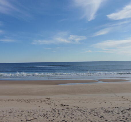 A calm sea with waves flowing onto the sand, forming a sandbar at the base of the beach