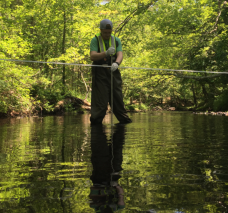 USGS scientist standing in a river collecting a water sample