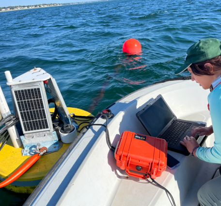 A woman types on her laptop on a boat next to a floating buoy.