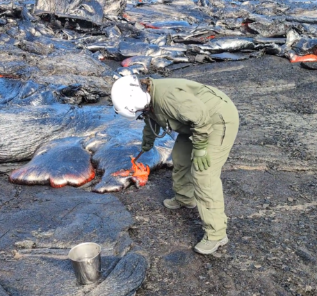 Color photograph of scientist collecting sample of lava
