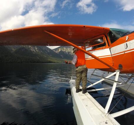 A scientist stands on a seaplane float and collects a water sample from a lake