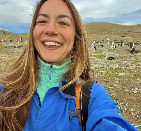 Selfie of bioloigist Seren Bagcilar with a  colony of penguins behind her