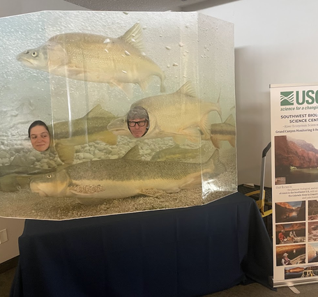 Two USGS scientists smile through a playful humpback chub cutout display