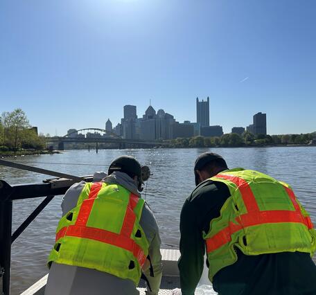 photograph of two men on a river with city skyline in background