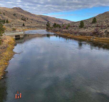 Small boat floats in river with dry grassy hills in background