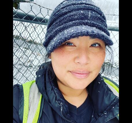 Headshot of a female wearing black snow dusted hat next tp a metal fence on a snowy day