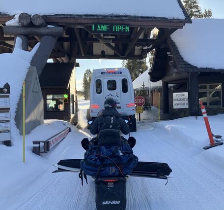 A person on a snowmobile waits behind an oversnow van at the park entrance station 