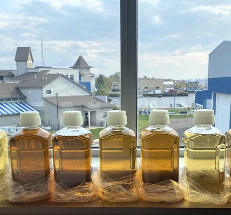 Nine clear bottles filled with colored water samples ranging from light yellow to brown sitting on a windowsill