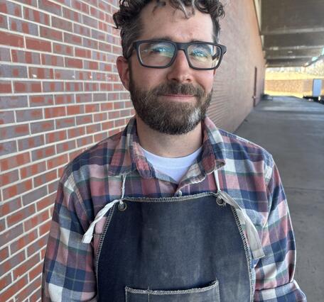Man with curly hair, glasses, and a flannel shirt. 