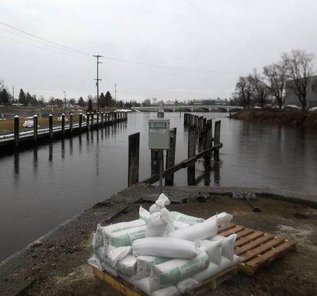 Streamgage at river with buildings on shore, sandbags in foreground