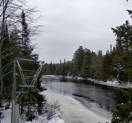 A gray metal cableway on the shore of a frozen river in winter