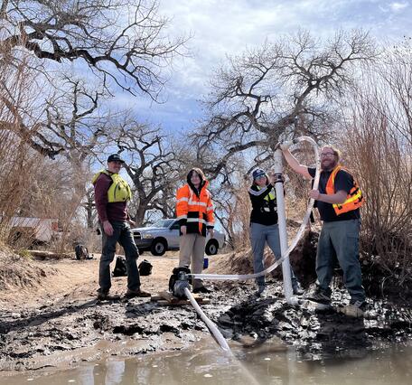 Four USGS employees stand on a riverbed, two of them holding a microplastics sampler. 