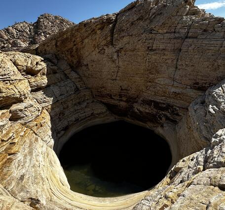 Round pool of water nestled among desert rocks beneath a clear blue sky.