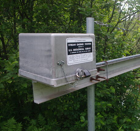View of streamgage equipment on side of river with USGS signeage