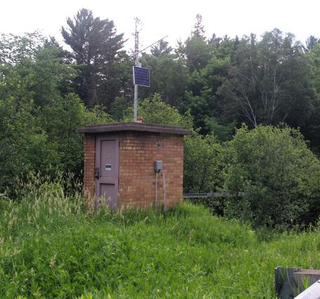 Brick streamgage house on bank of river next to rural country road in summertime