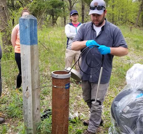 A man conducts a groundwater well monitoring demonstration in a grassy area