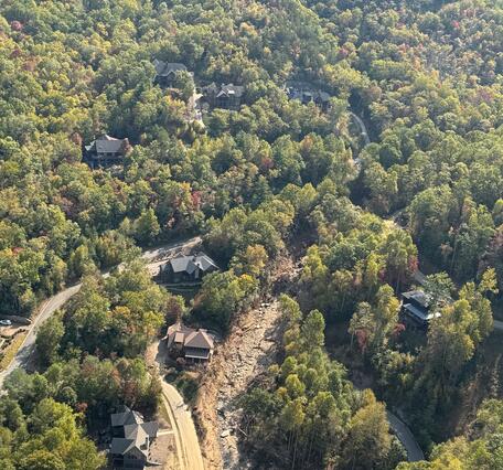 aerial view of forested area with landslide path visible near houses and road