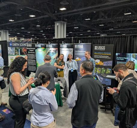 USGS employees smile while standing behind a booth at a conference