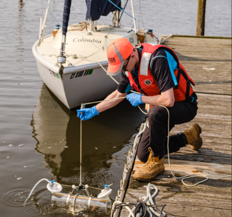 A hydrologic technician drops a water quality sampler into a river from a dock. 