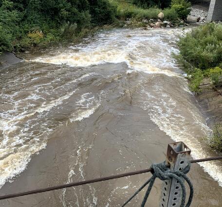 A bright orange acoustic Doppler current profiler takes a streamflow measurement in a flooded stream