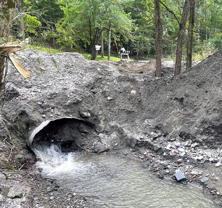 Clogged culvert pipe filled with sediment and some water running out of it.