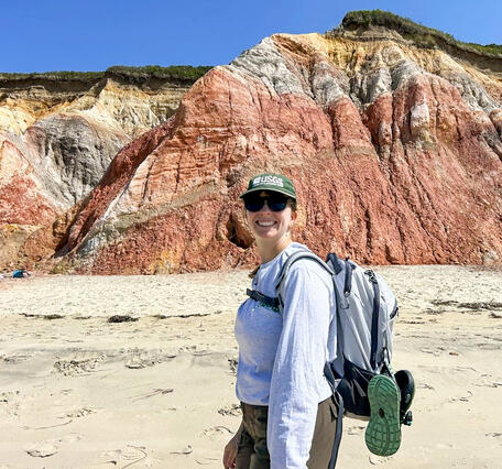 Geographer and drone pilot stands in front of a colorful section of cliffs.