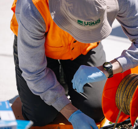 scientist looks at watch while lowering tape into well