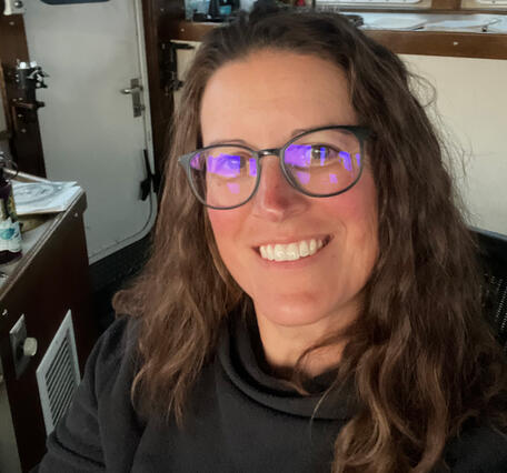 A researcher sitting on the bridge of a large vessel. Lake in the background.
